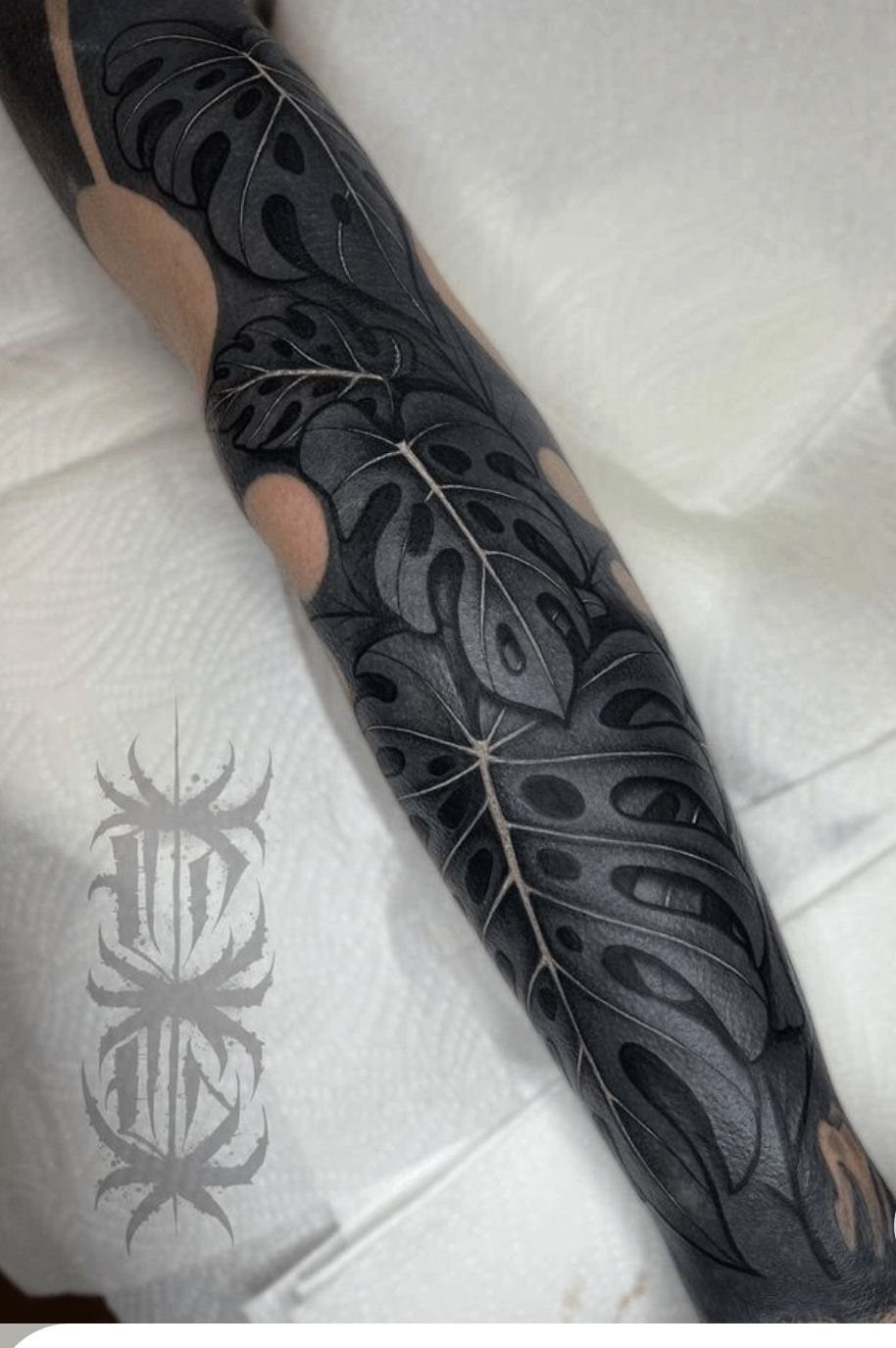 Botanical Tattoo Blackwork: 8 Ideas for Ink That Grows on Skin 8 A large blackwork tattoo of monstera leaves covering a person's arm.