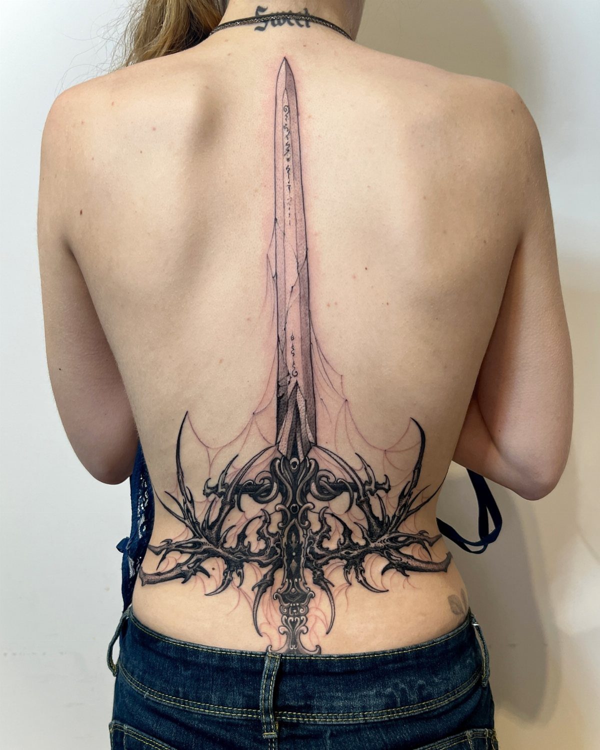 12 Back Tattoo Goth Styles for Spine, Skulls, and Full Backpieces 5 A vertical neotribal gothic sword tattoo with thorny patterns on a person's back.