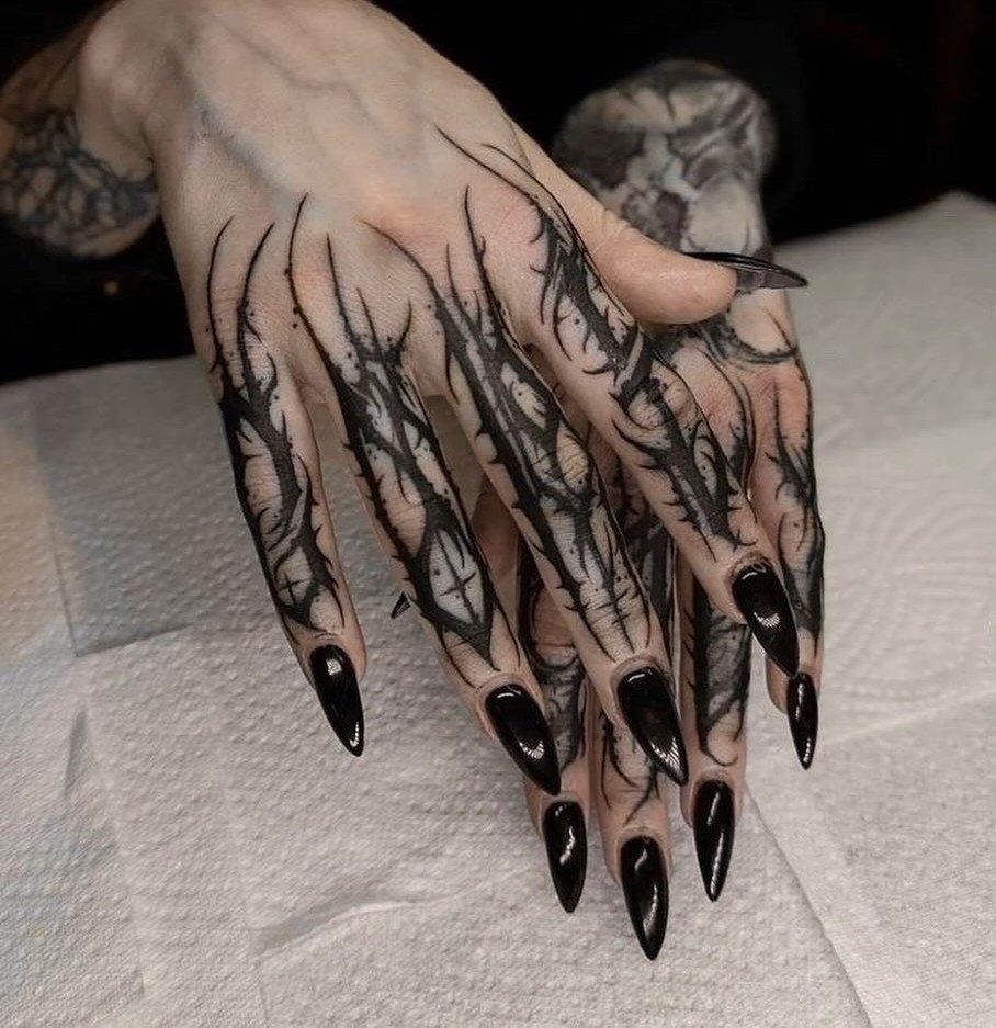 Hands with long black nails featuring intricate black organic tribal tattoos on the fingers.