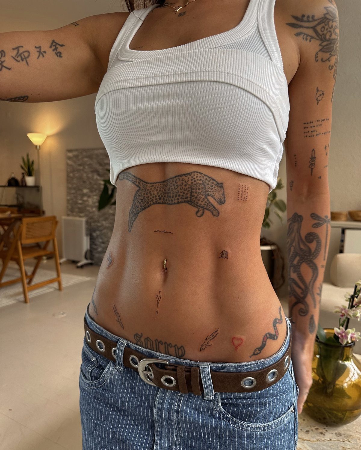 A person with various small black ink tattoos on their stomach, ribs, and arms.