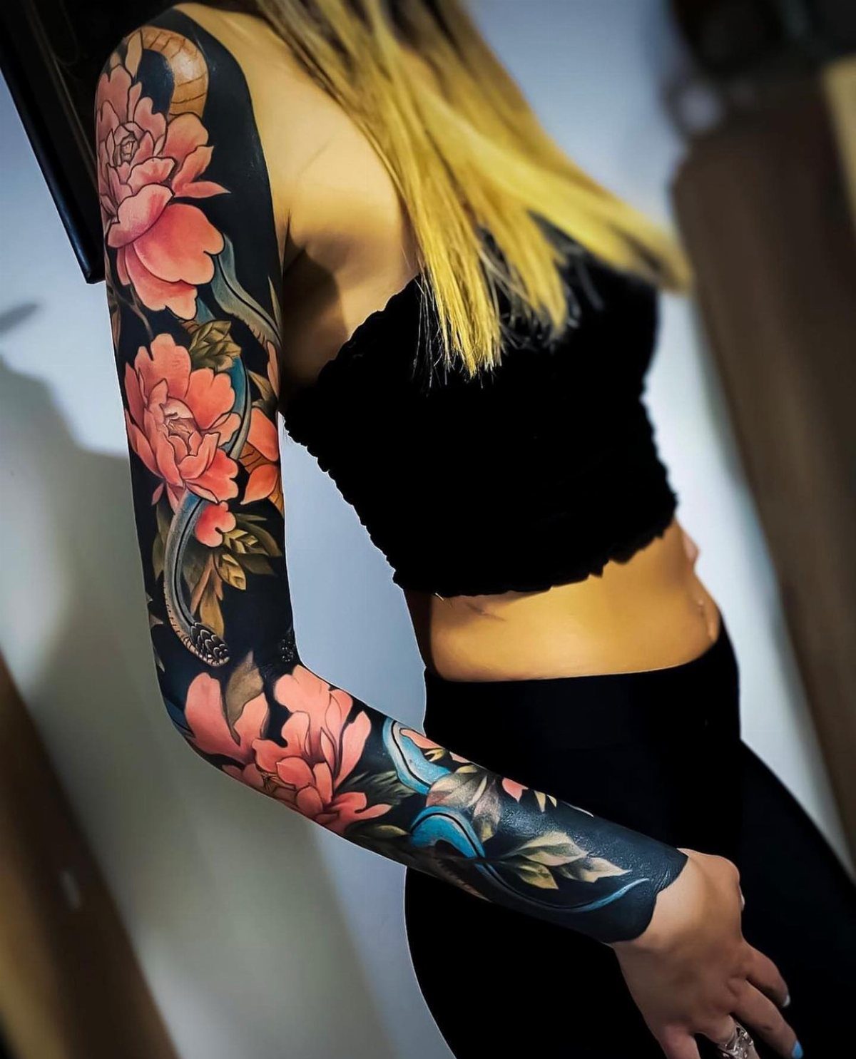 Japanese Tattoo Style: 14 Iconic Motifs and Where They Go 7 A person's arm featuring a large, colorful sleeve tattoo of pink peony flowers and green leaves.
