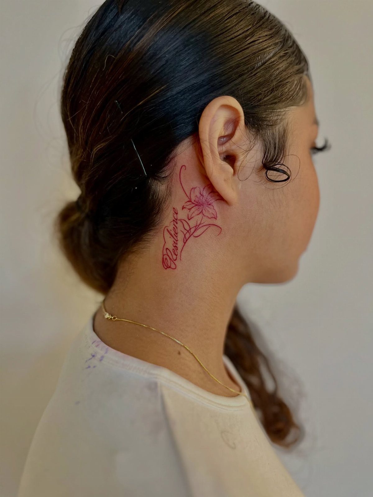 A woman with a red floral tattoo on the skin behind her ear and neck.