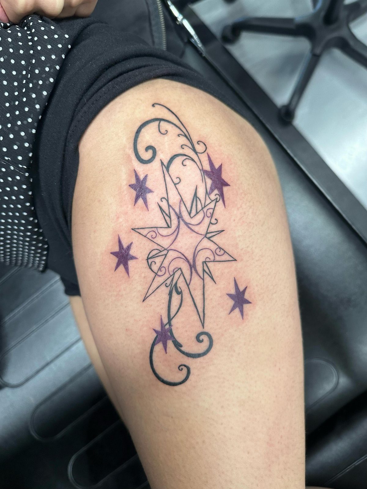 A large purple star tattoo with black swirls and smaller stars on a person's thigh.