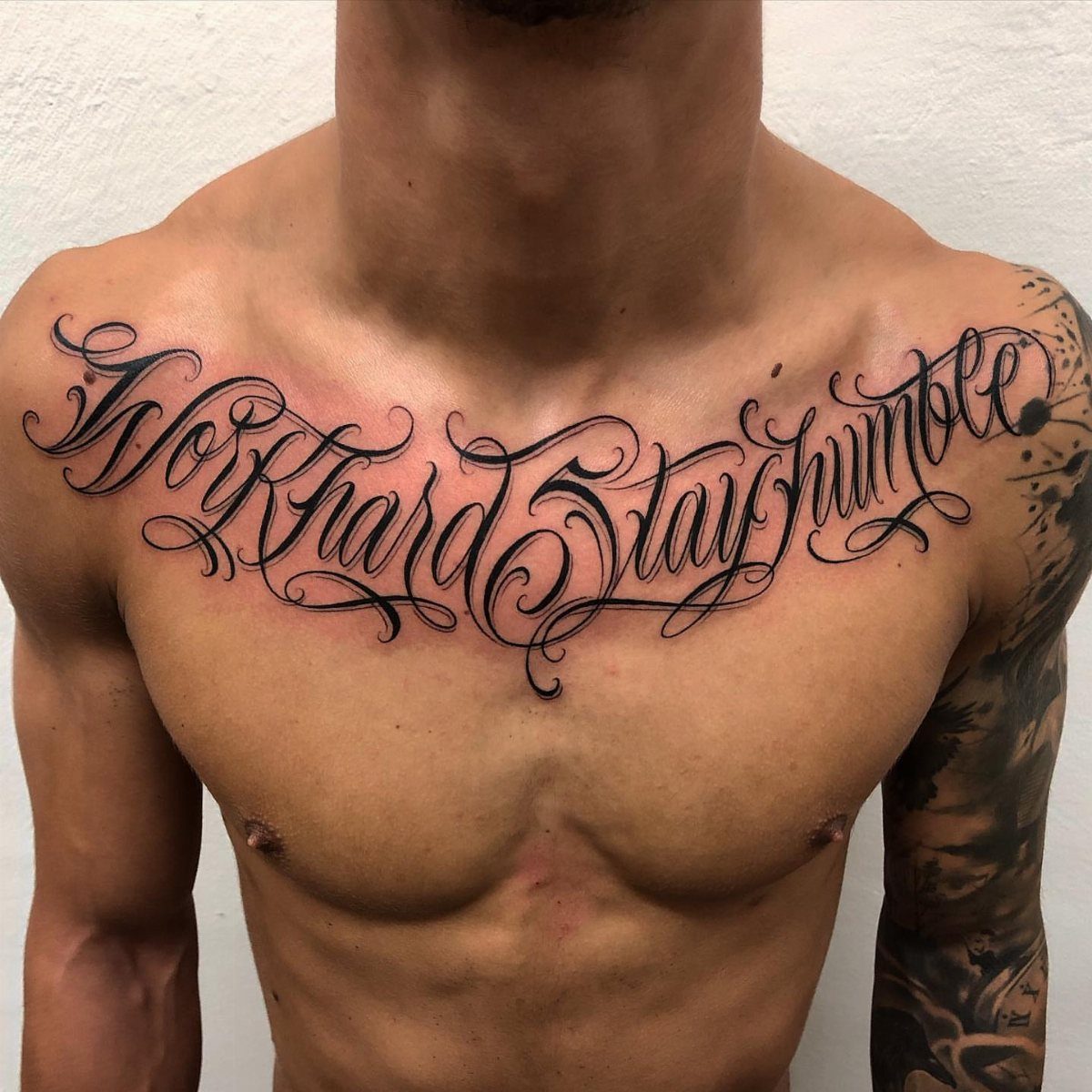 Tattoo at Chest: 15 Ideas from Wing Spread to Underboob 10 A man's chest featuring a large black script tattoo that reads Work Hard Stay Humble.
