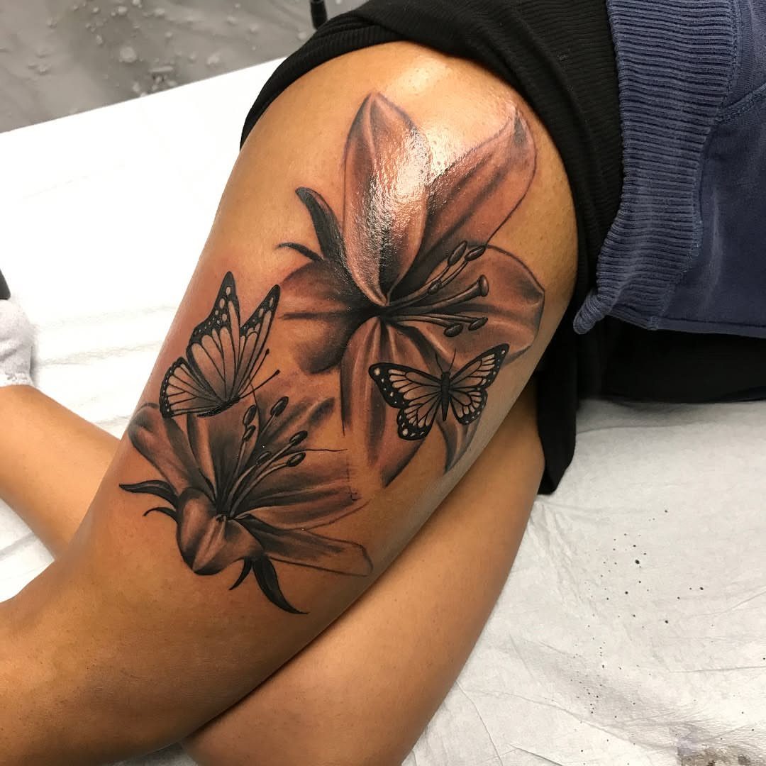 Black and grey lily and butterfly tattoo on a person's side thigh.