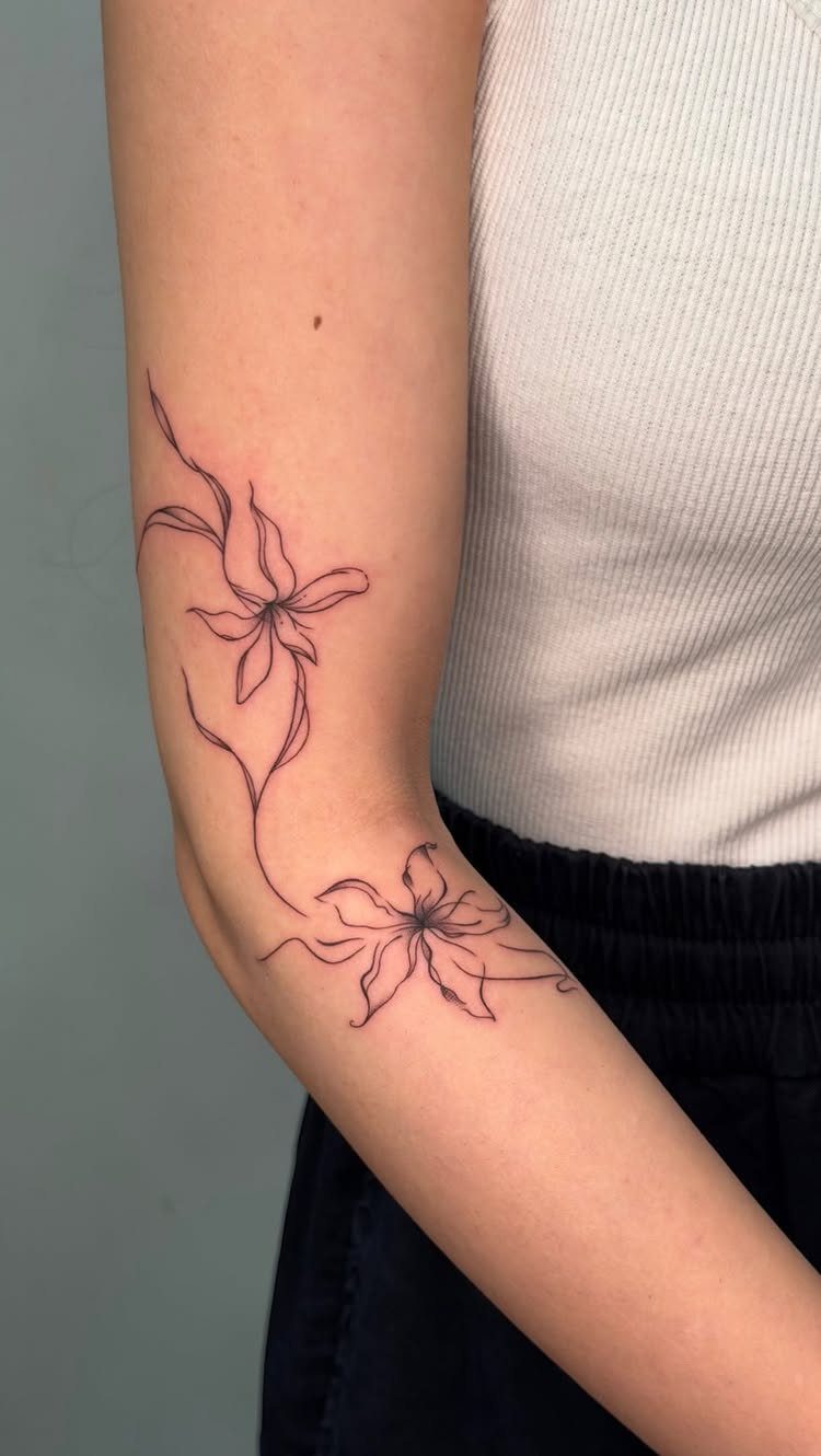Minimalist fine line flower tattoos on a person's arm with flowing stems.
