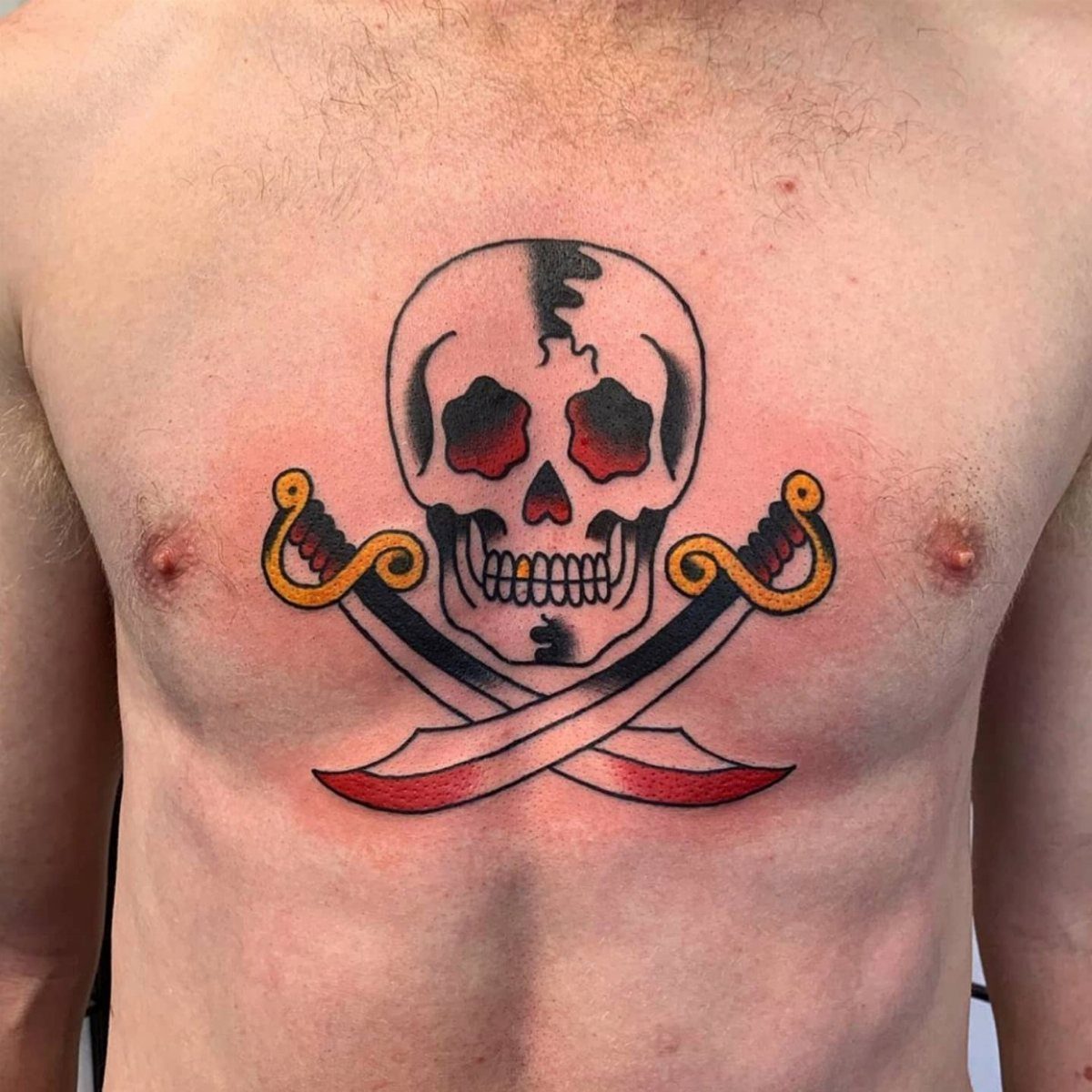 Tattoo at Chest: 15 Ideas from Wing Spread to Underboob 6 A skull tattoo with crossed swords positioned on a man's chest.