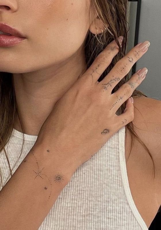 A person's hand and wrist decorated with various small, fine line celestial symbol tattoos.
