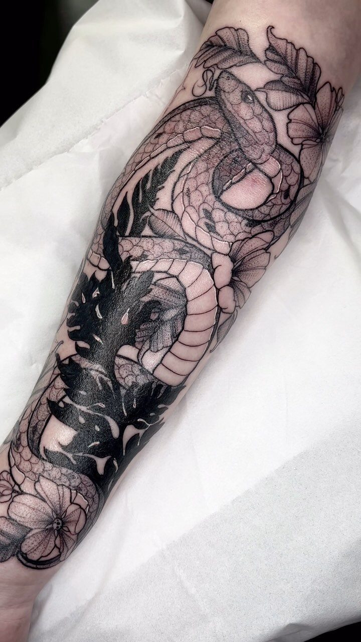 Botanical Tattoo Blackwork: 8 Ideas for Ink That Grows on Skin 9 A large blackwork tattoo of a snake and botanical leaves on a person's forearm.