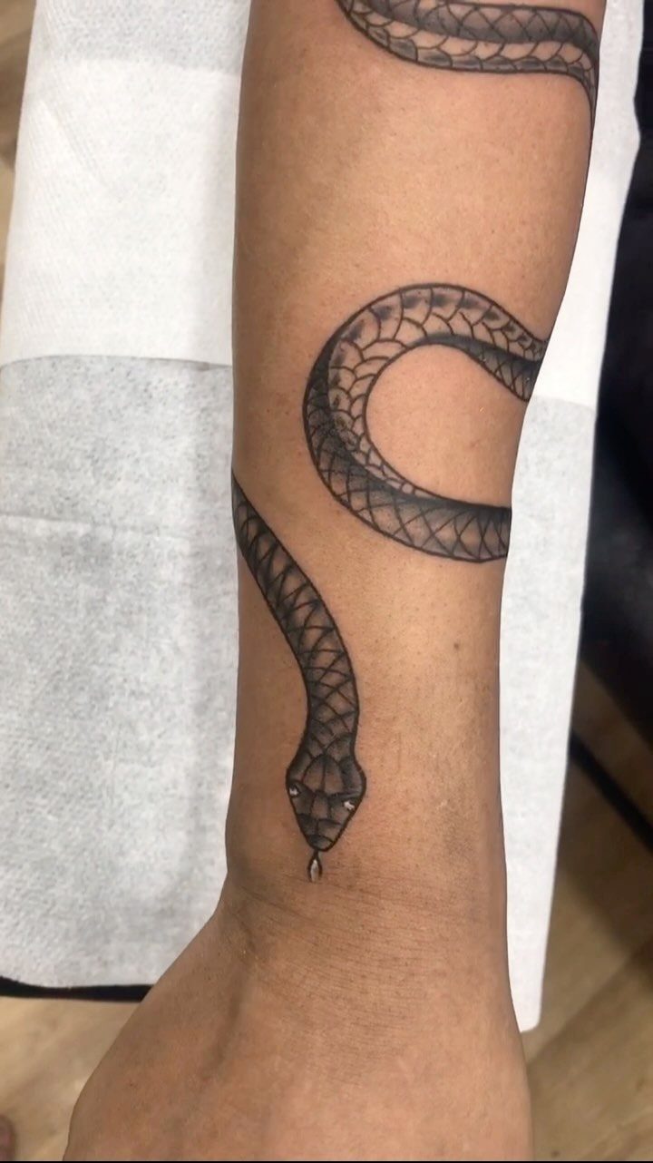 11 Tattoo Arm Women Will Want to See Before Booking 2026 3 A black ink snake tattoo winding around a person's forearm with detailed scale patterns.