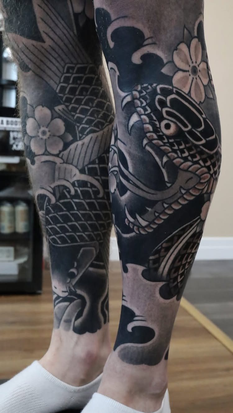 Japanese Tattoo Style: 14 Iconic Motifs and Where They Go 12 A person's legs covered in large black and grey Japanese style tattoos including a snake and koi fish.