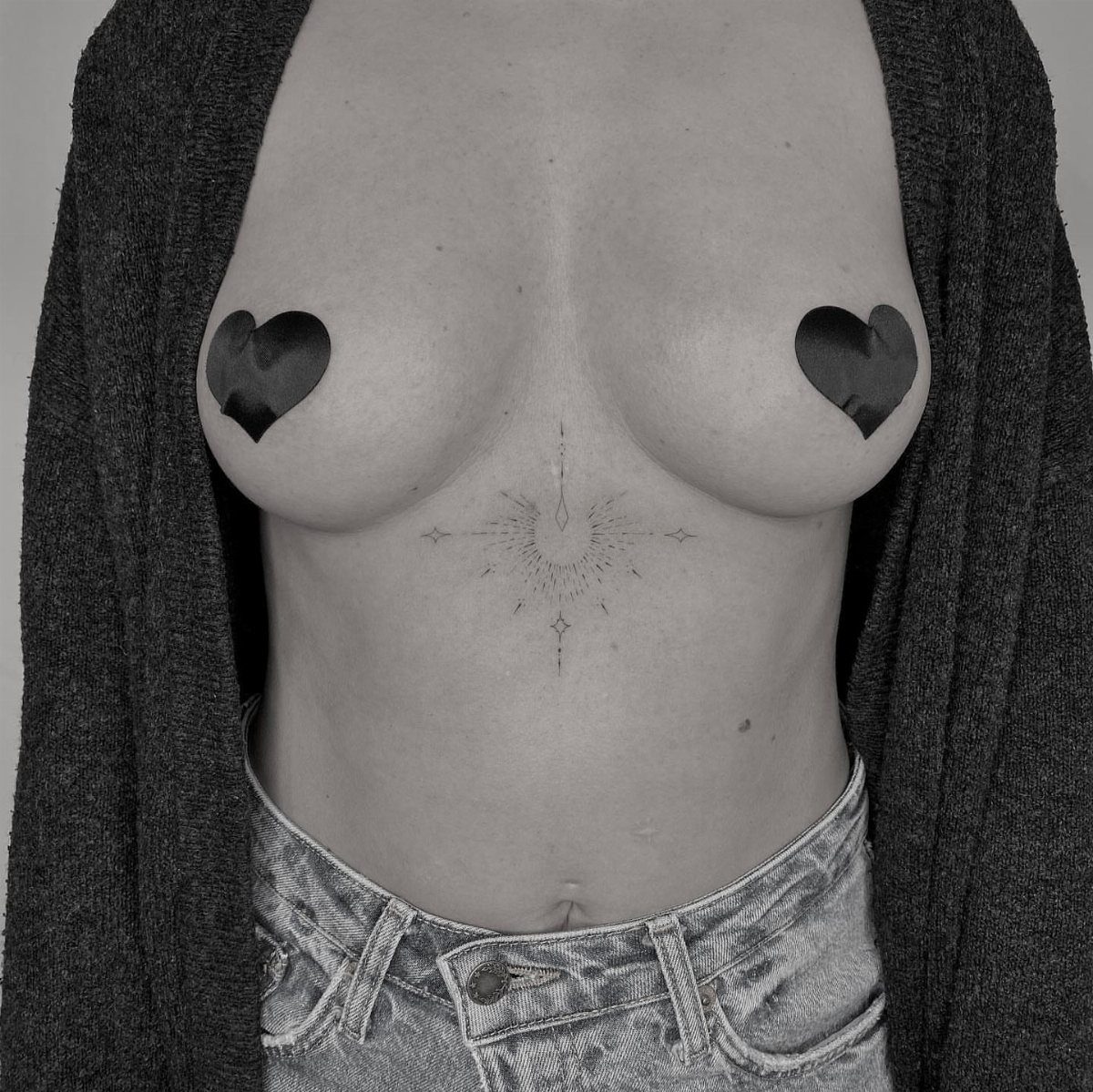 14 Places for a Tattoo for Women: From Ankle to Neck 12 A woman with a sunburst tattoo on her sternum and heart shapes over her breasts.