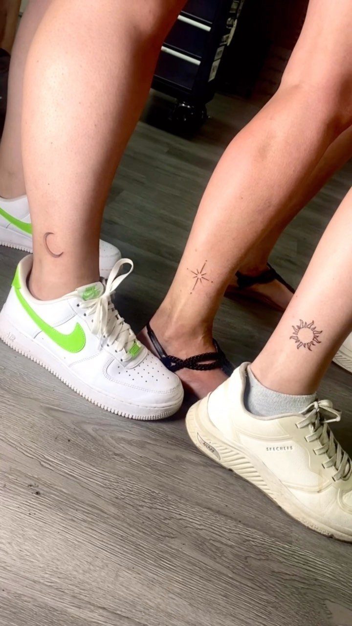 Three ankles showing small black tattoos of a moon, a star, and a sun.