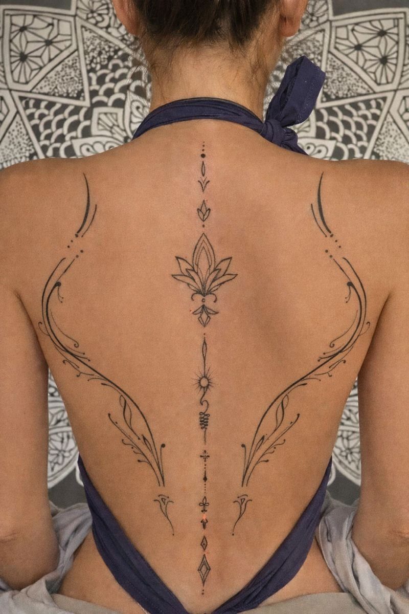 A person's back displaying a large, symmetrical black ink tattoo with fine lines and organic shapes.
