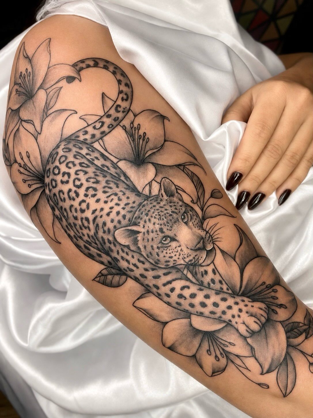 A large leopard and lily tattoo on a woman's upper arm with white satin fabric.