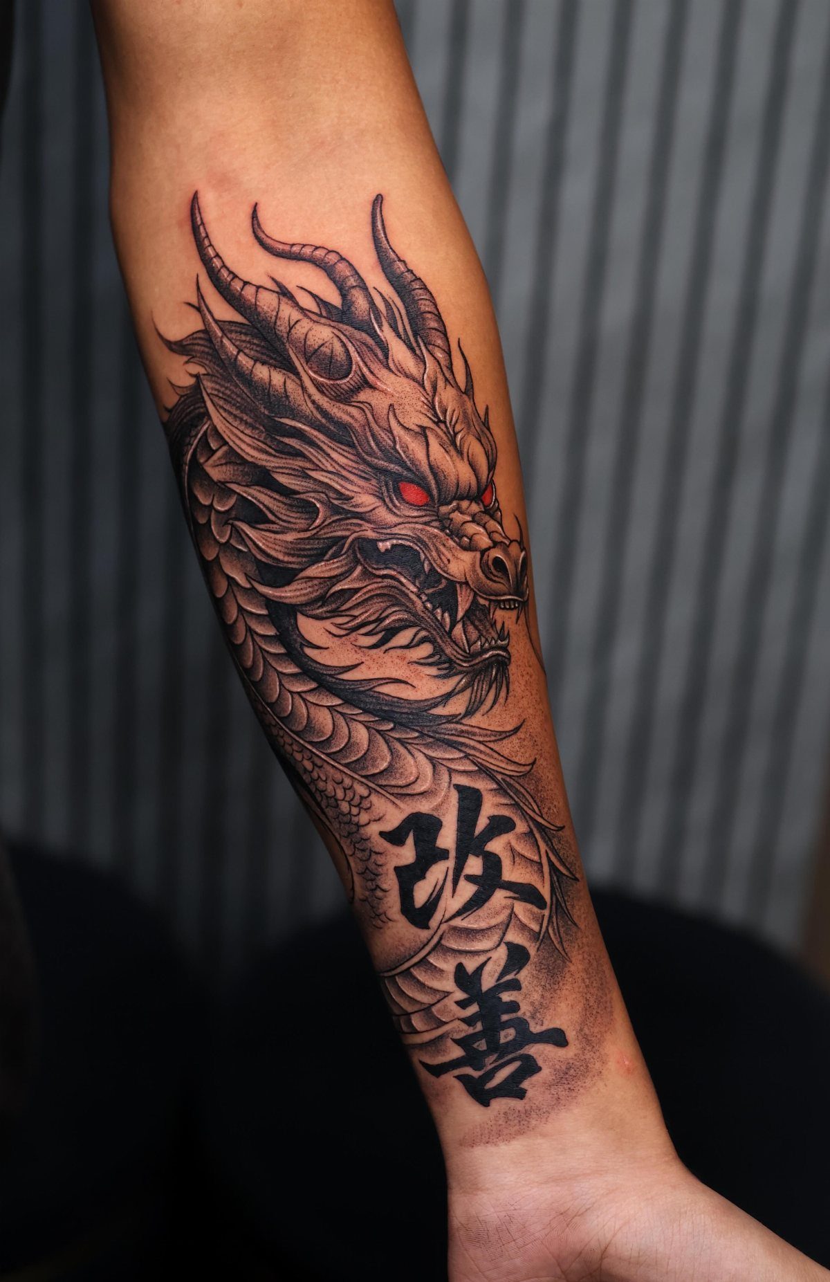 A detailed black and grey dragon tattoo with red eyes on a person's forearm.