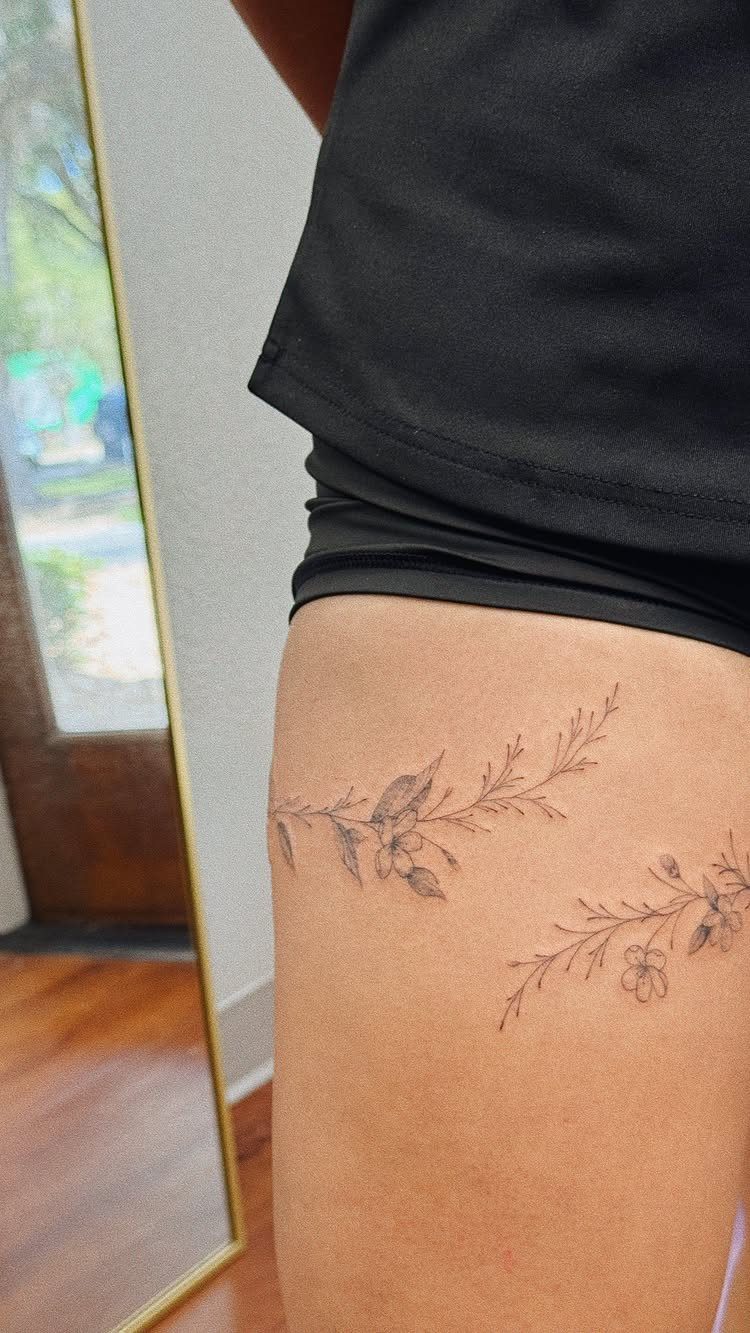 Fine Line Tattoo Placement: 11 Ideas That Actually Work 4 Fine line floral tattoos on a person's thigh with delicate branches and small flowers.