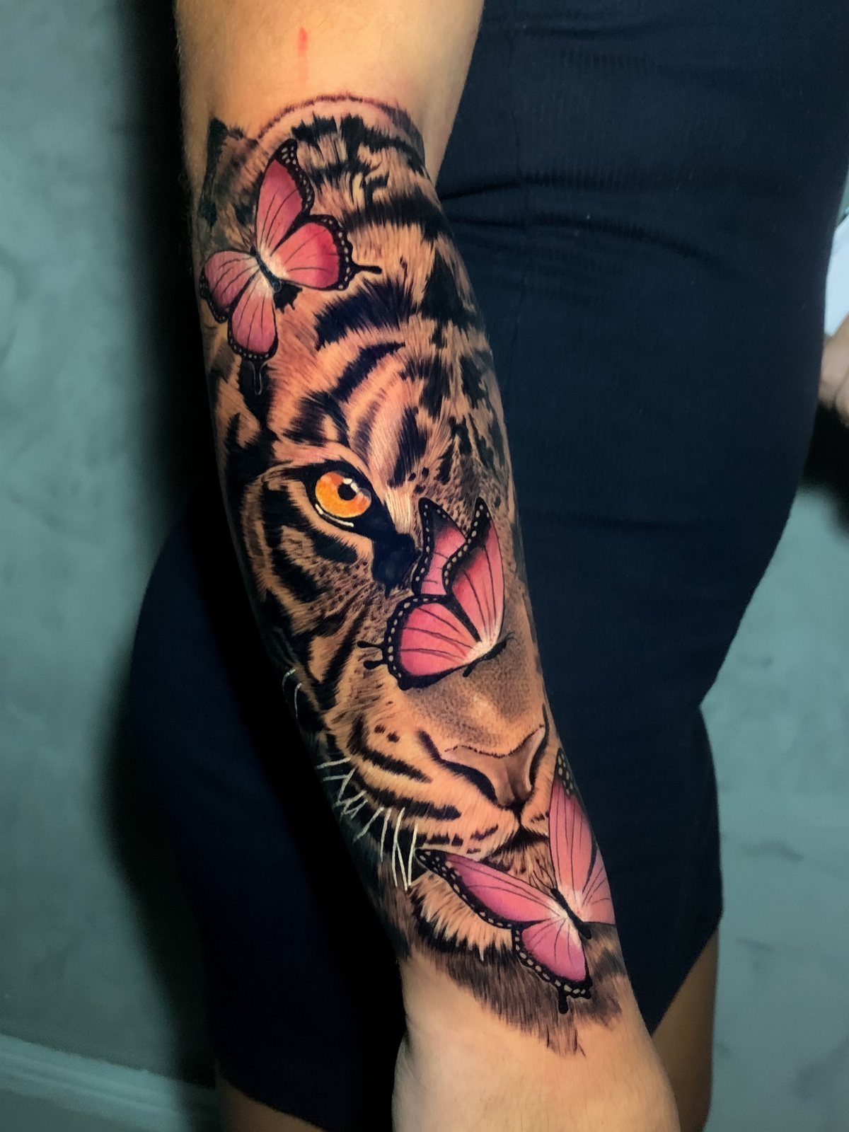 11 Tattoo Arm Women Will Want to See Before Booking 2026 6 A detailed tiger tattoo with pink butterflies on a woman's forearm.