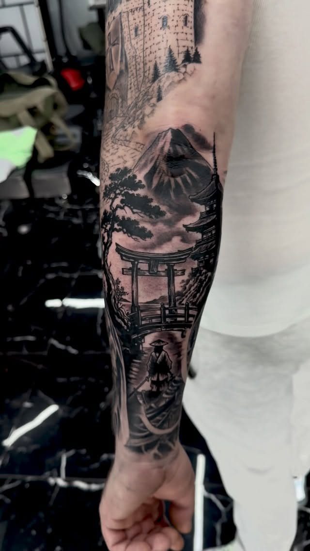 Japanese Tattoo Style: 14 Iconic Motifs and Where They Go 10 A detailed black and grey tattoo on an arm depicting a mountain, pagoda, and torii gate.