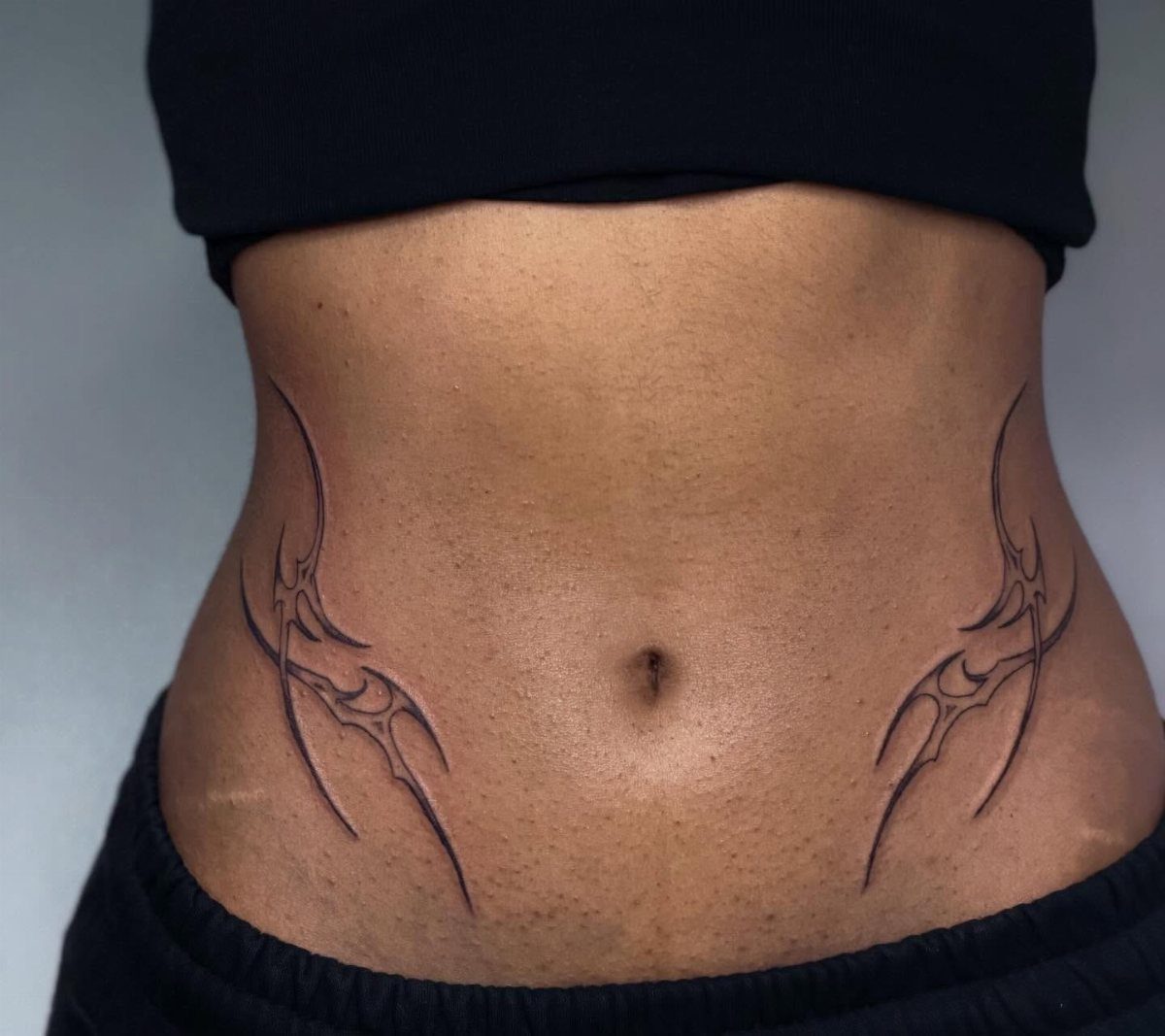 Two symmetrical tribal tattoos curving along the sides of a person's stomach and waist.