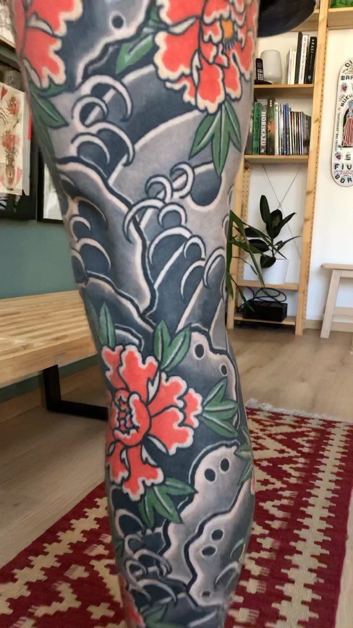 Japanese Tattoo Style: 14 Iconic Motifs and Where They Go 9 A large Japanese style tattoo on a leg featuring red peonies and grey waves.