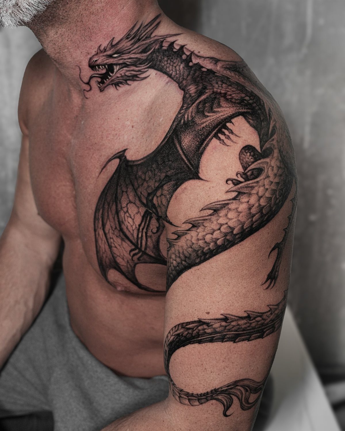 Tattoo Pattern Dragon: 11 Ideas for Ink That Follows the Body 4 A large black ink dragon tattoo with bat-like wings covering a man's neck, chest, and shoulder.