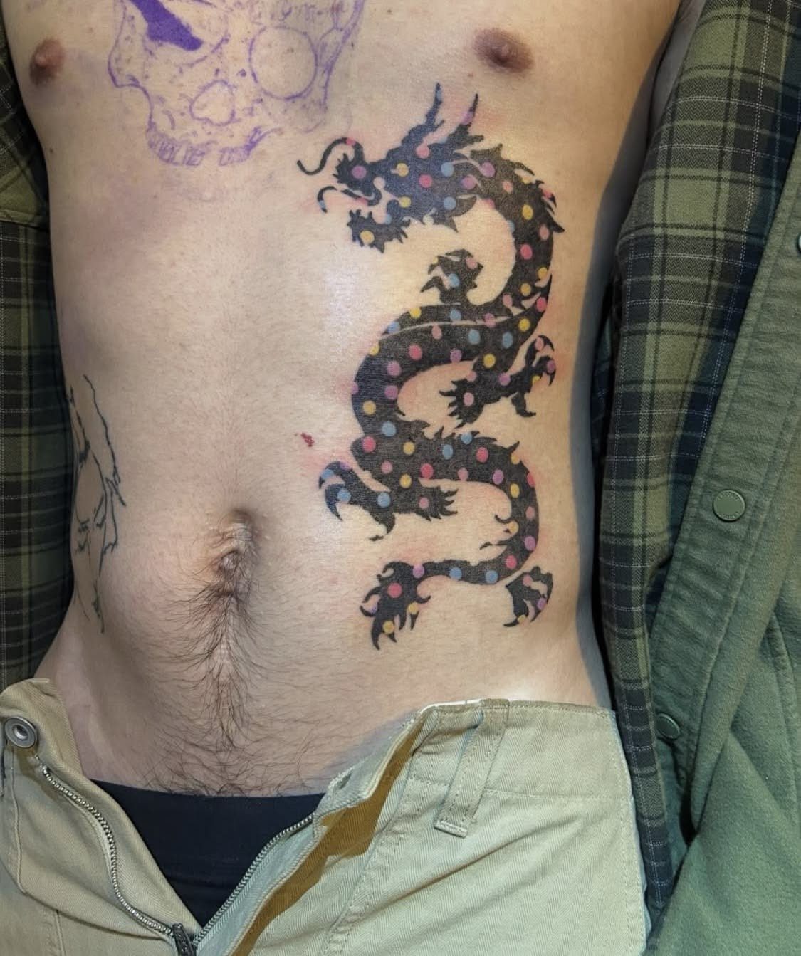 Tattoo Pattern Dragon: 11 Ideas for Ink That Follows the Body 12 A colorful polka-dotted dragon tattoo applied to the side of a person's abdomen.