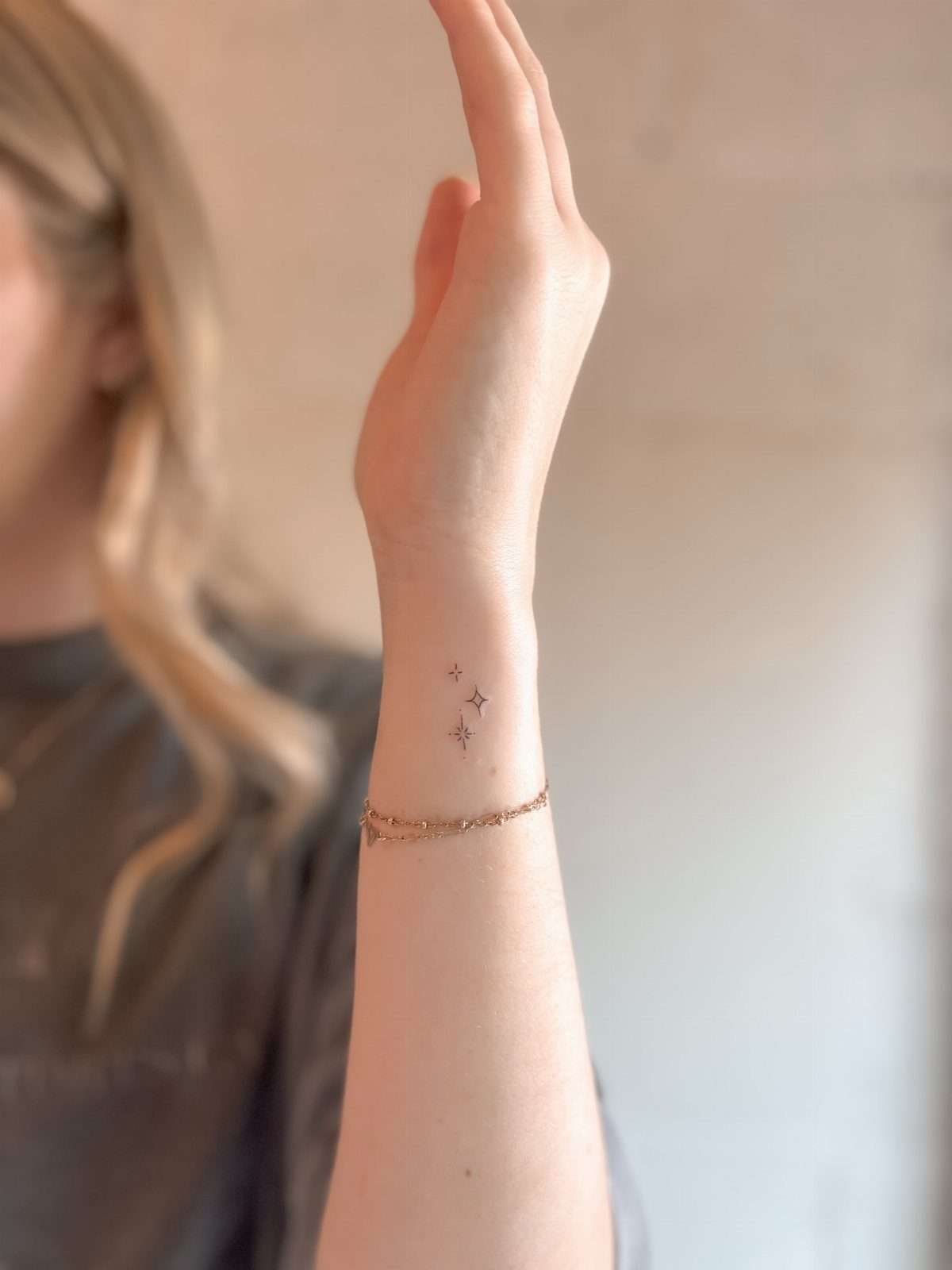 Fine Line Tattoo Placement: 11 Ideas That Actually Work 6 A person's wrist featuring two small fine line star tattoos and a gold bracelet.